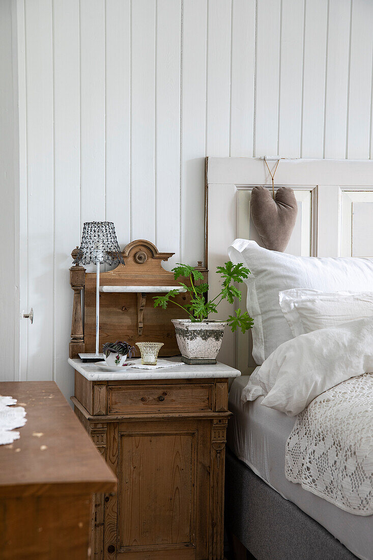 Antique wooden bedside cabinet with plant and decorative lamp in the bedroom