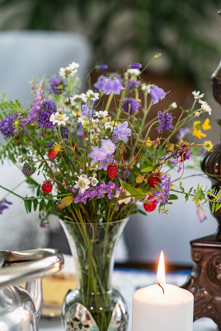 Blumenarrangement mit Wildblumen und brennende Kerze auf dem Tisch