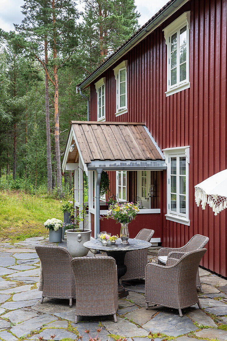 Patio seating area with rattan furniture in front of red wooden house in the forest