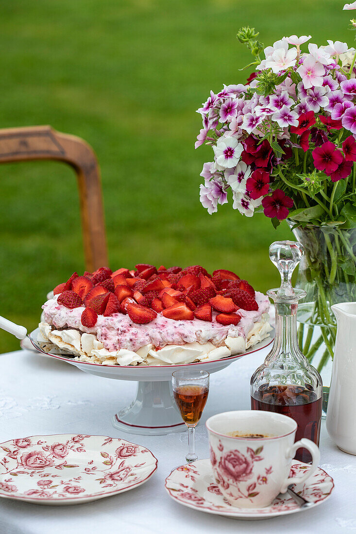 Erdbeertorte, Kaffeeservice und Petunienstrauß auf Gartentisch