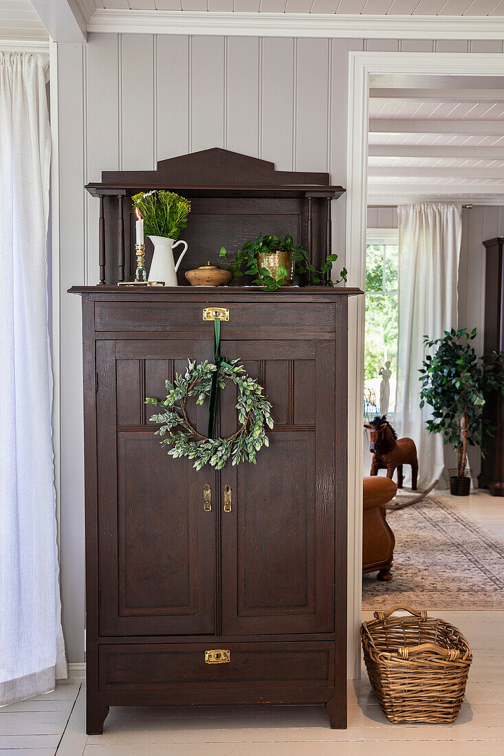 Dark wooden cabinet with decorative wreath in a light-colored room