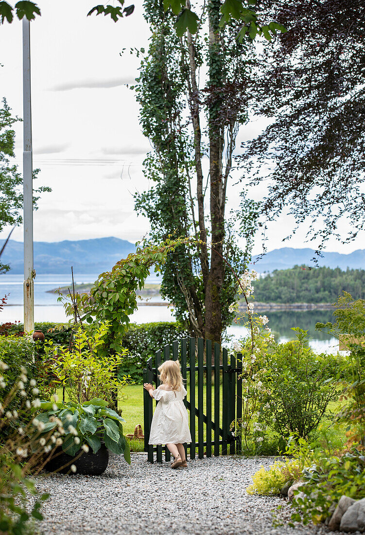 Child playing in garden with lake view and green gate