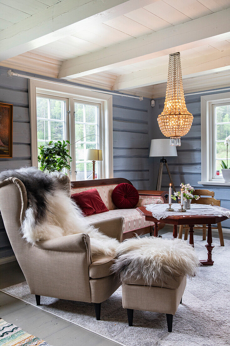 Cozy sitting area with wing chair and sofa under chandelier in wooden house