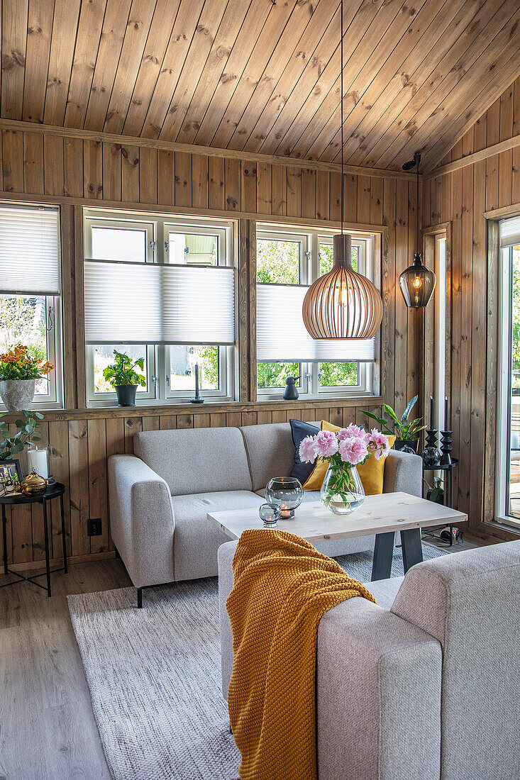 Graue Sofas und Holztisch mit Blumenstrauß in holzvertäfeltem Wohnzimmer