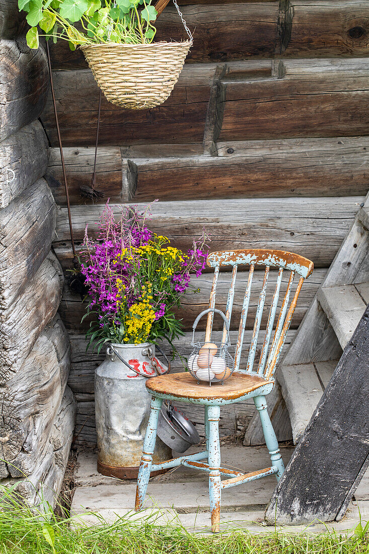 Wooden stool in shabby chic look in front of wooden wall, milk jug with wildflower bouquet