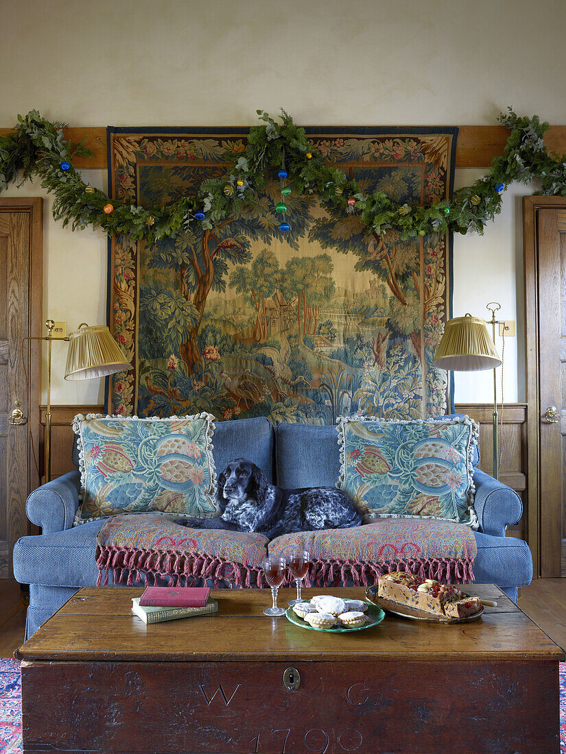 Weihnachtliches, rustikales Wohnzimmer mit Wandteppich und Holzmöbeln, Hund entspannt auf Sofa