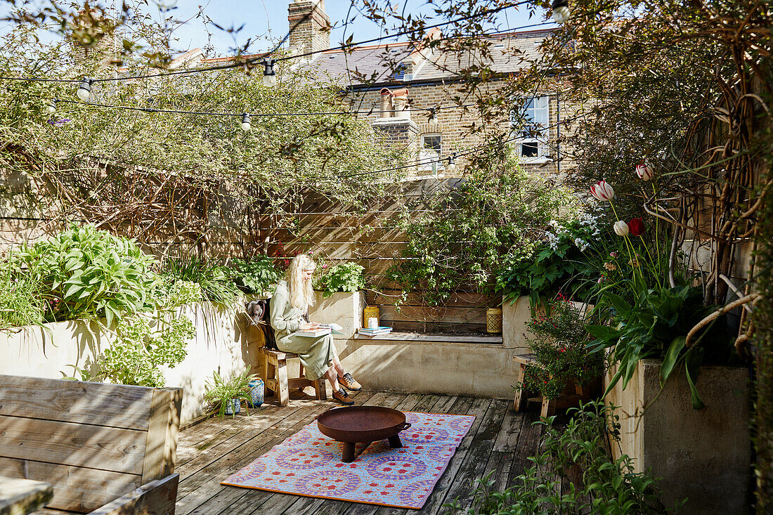 Idyllic, urban backyard garden with wooden deck and plants, woman in the background