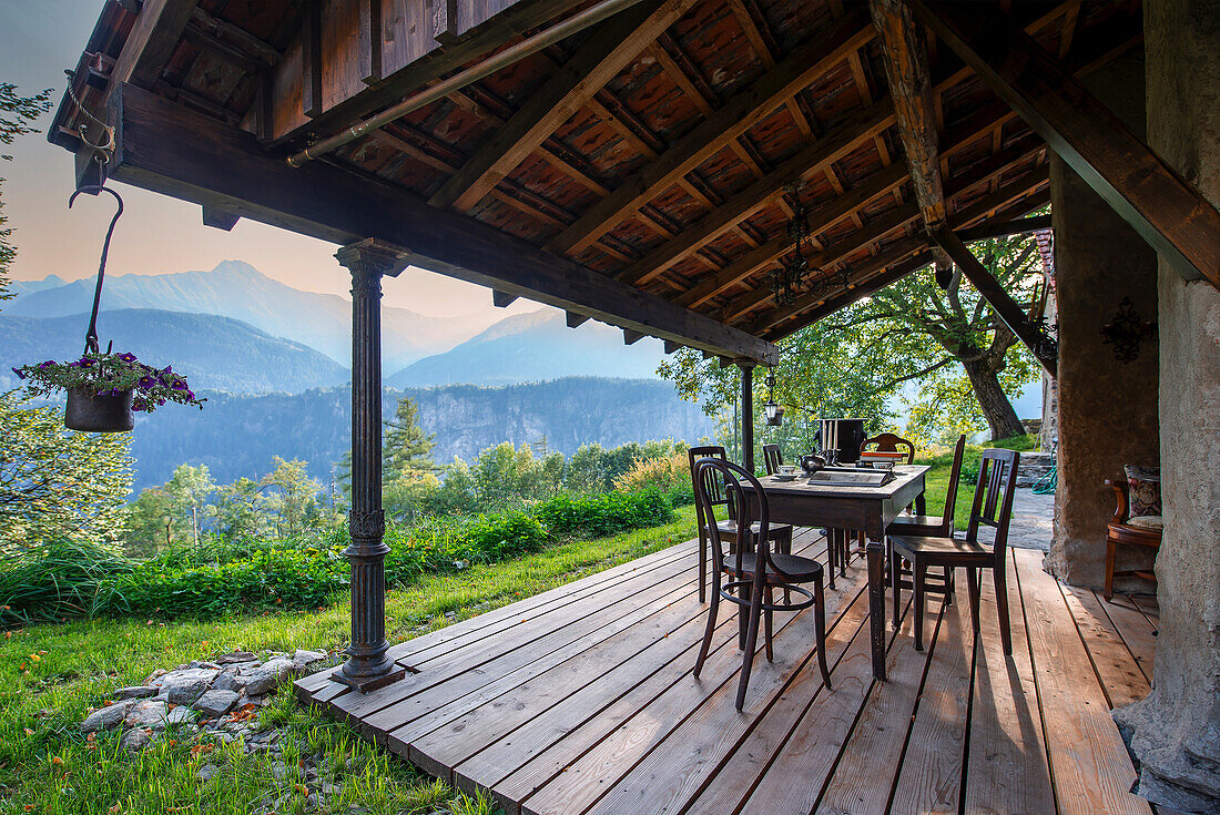 Covered wooden terrace with dining table and chairs, mountain landscape in the background