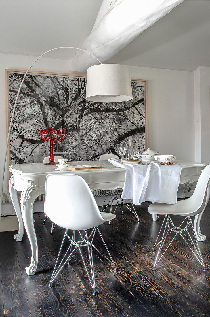 White dining table with curved legs and white Eames chairs in front of a large tree photo