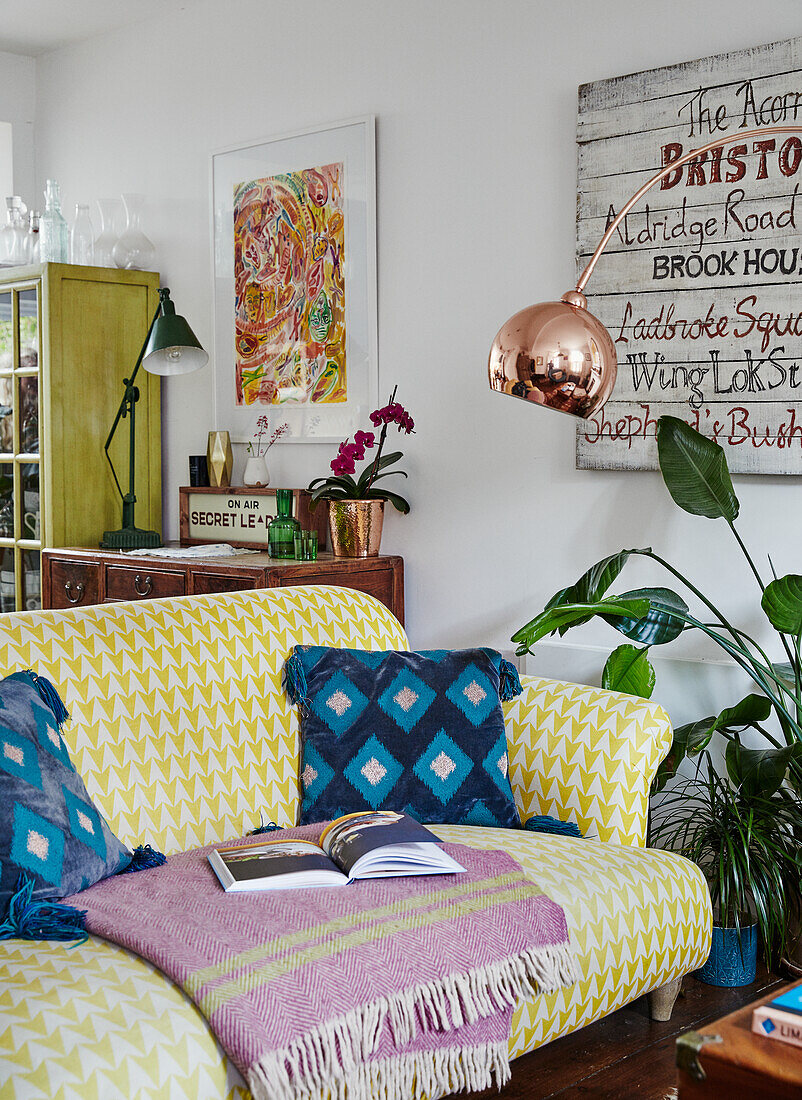 Gemusterte gelbe Couch mit Decke, Kunstwerke an der Wand, Vintage-Elementen und Zimmerpflanzen