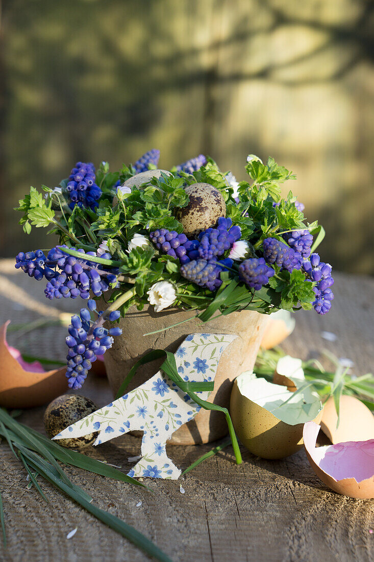 Osterdekoration mit Traubenhyazinthen (Muscari), Wachteleiern, Eierschalen und DIY-Vogelanhänger auf Holzuntergrund