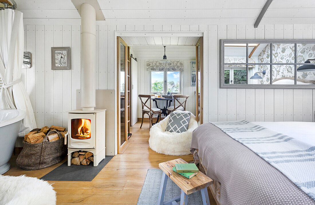 Open bedroom with white wood-burning stove and dining area in the background