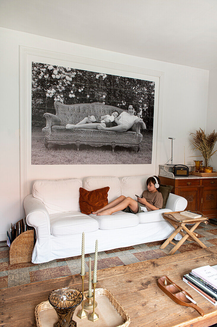 Kind sitzt auf weißem Sofa vor Kunstfotografie im Wohnzimmer