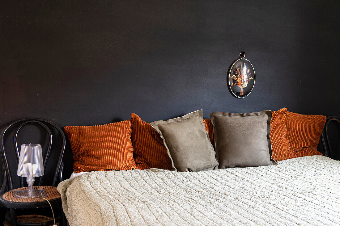 Schlafzimmer mit Bett und Zierkissen in Orange und Braun vor schwarzer Wand