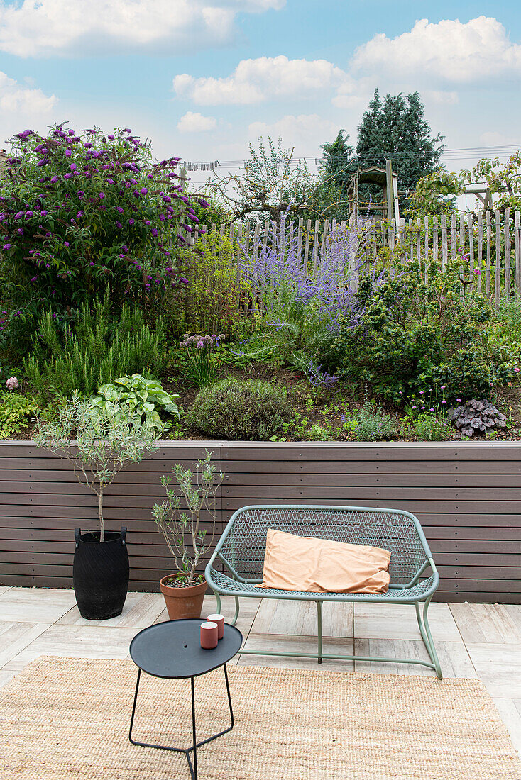 Terrasse mit Metallbank und Beistelltisch, Blick auf blühenden Garten