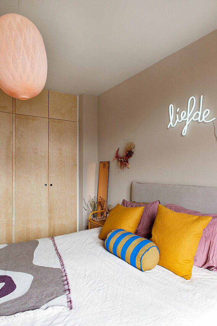 Bedroom with neon-lit liefde lettering and light-colored built-in wardrobe