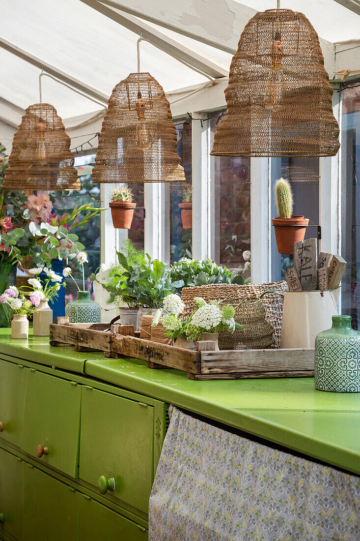 Wicker pendant lights above a green sideboard with houseplants and decorative elements