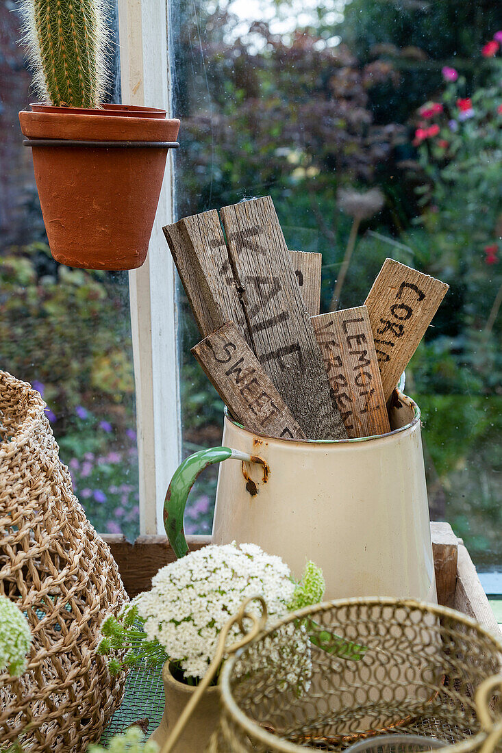Wooden signs with herb names in enamelled jug on windowsill