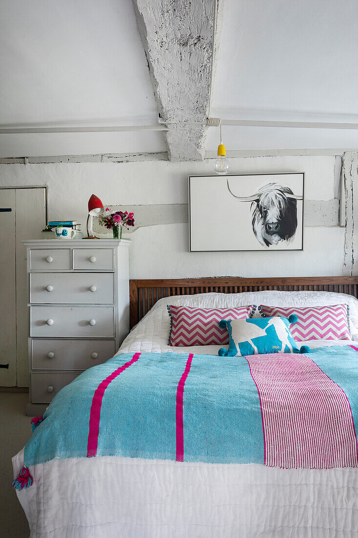 Schlafzimmer im Landhausstil mit Holzbett, gemusterter Bettwäsche und Wandbild