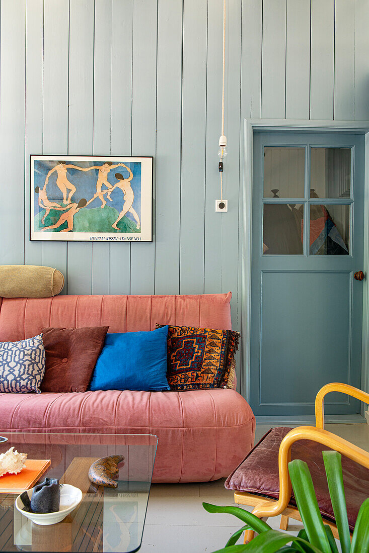 Living room with pink sofa and colorful pillows against a light blue wooden wall