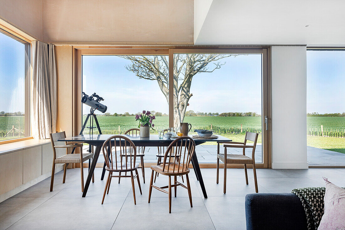 Dining room with large windows, wooden table and chairs, view of the countryside