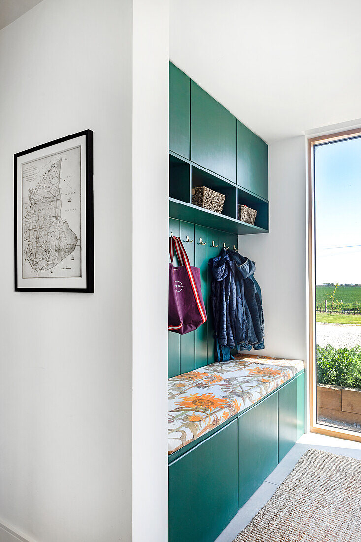 Green wardrobe with storage space and integrated bench with floral patterned upholstery