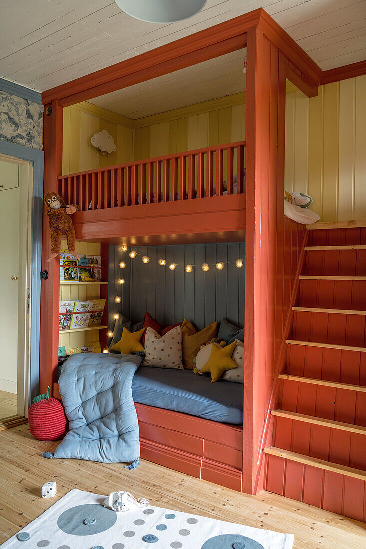 Red-painted loft bed with stairs, fairy lights and bookshelf in the children's room