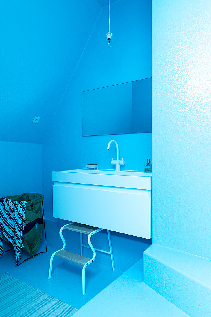 Minimalist blue bathroom with white washbasin and stool