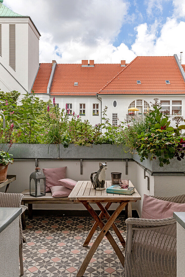 Small city balcony with wooden table, bench and flowering plants