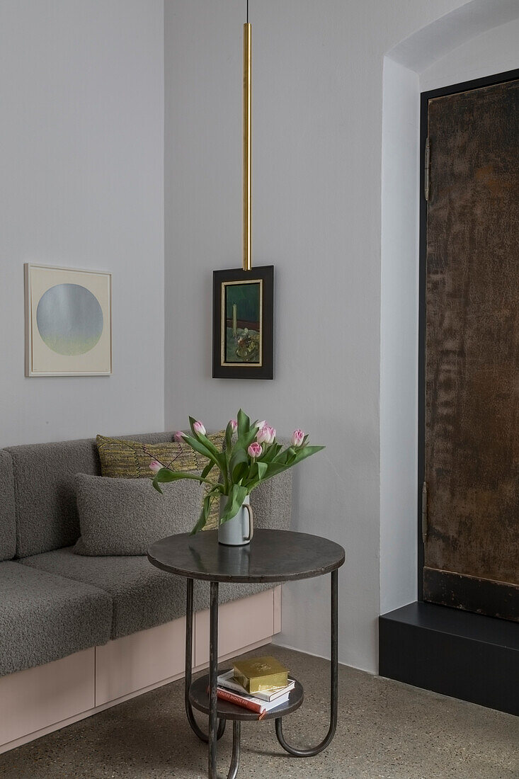 Round side table with tulip vase in front of grey corner sofa