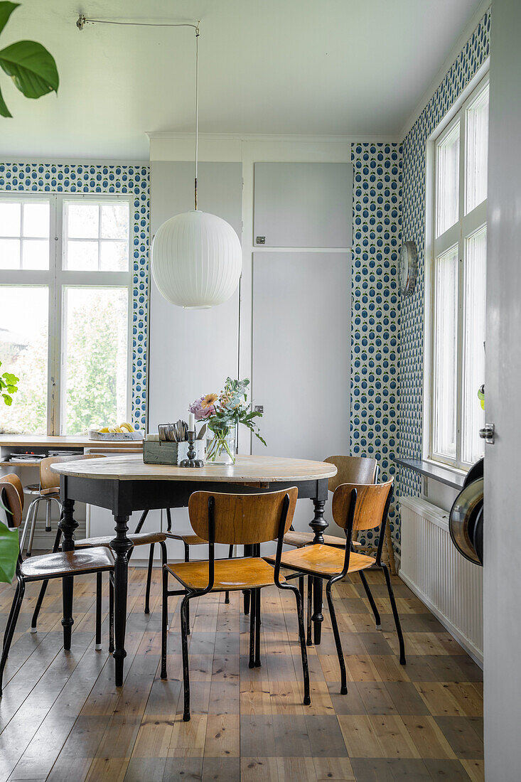 Dining room with patterned wallpaper, round wooden table and vintage chairs