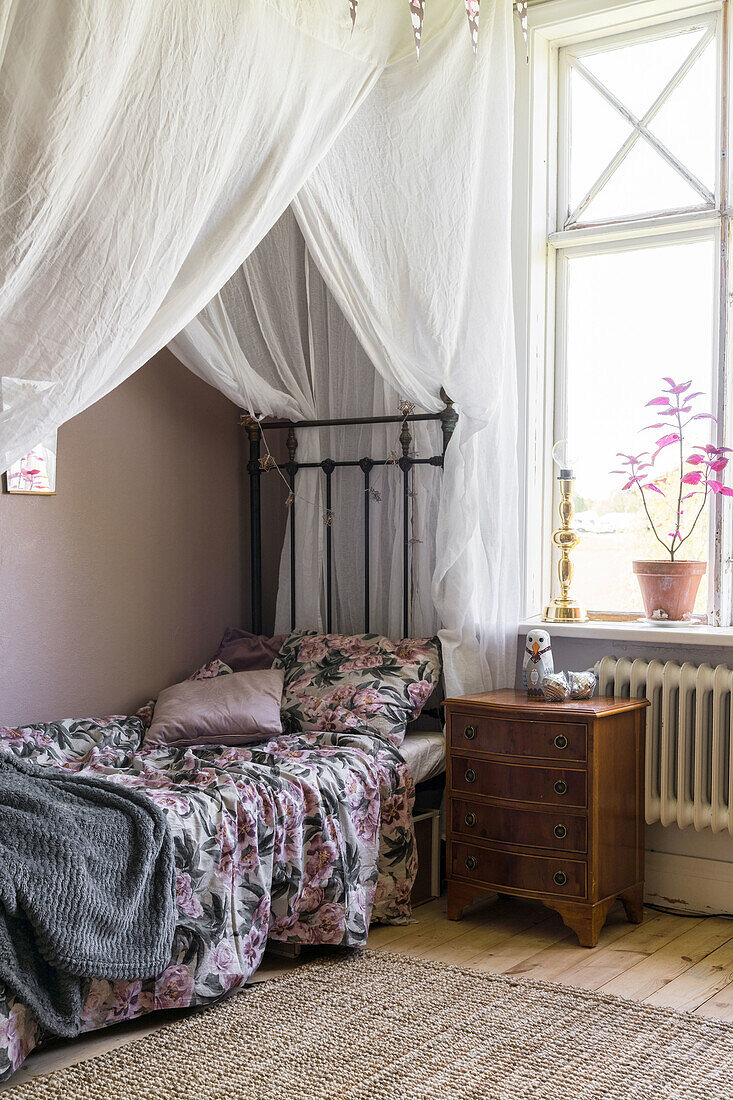 Metal single bed with floral bedding and canopy bed curtain