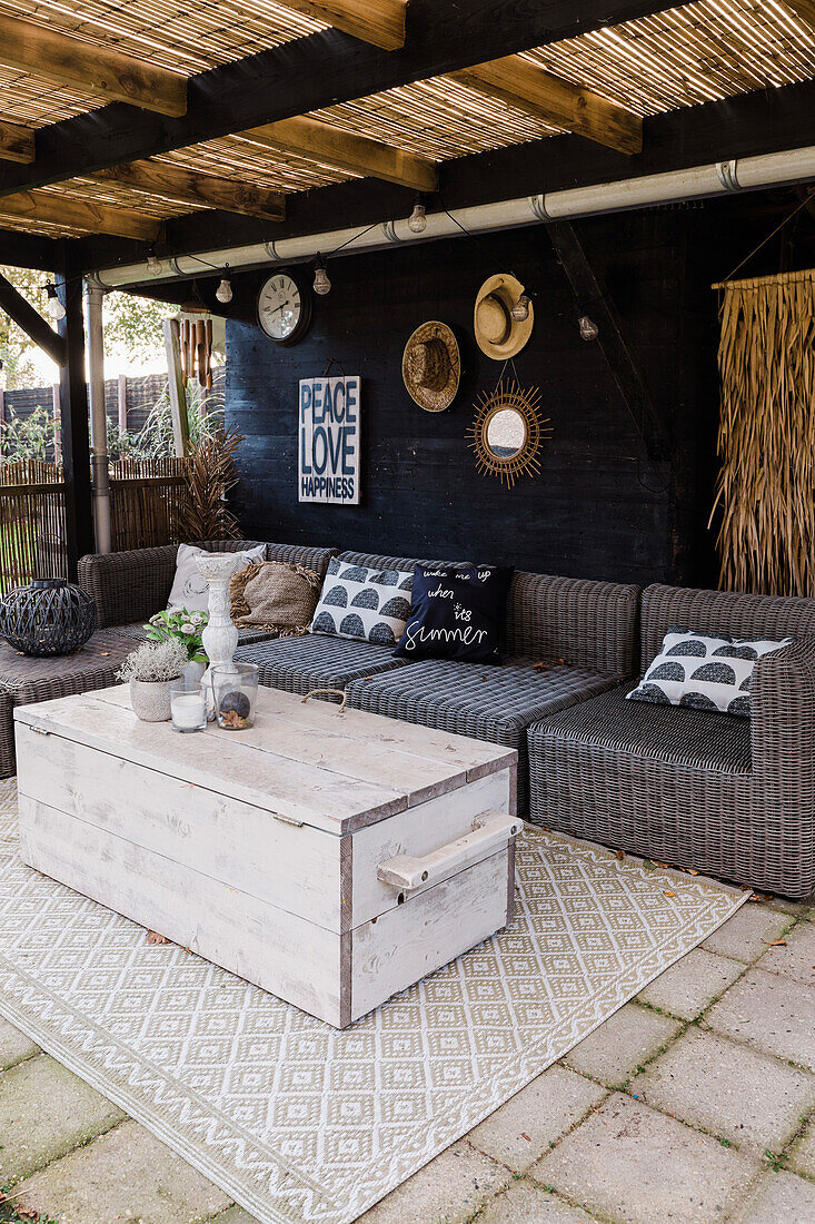 Überdachte Terrasse mit Rattansofa und rustikaler Truhe als Couchtisch