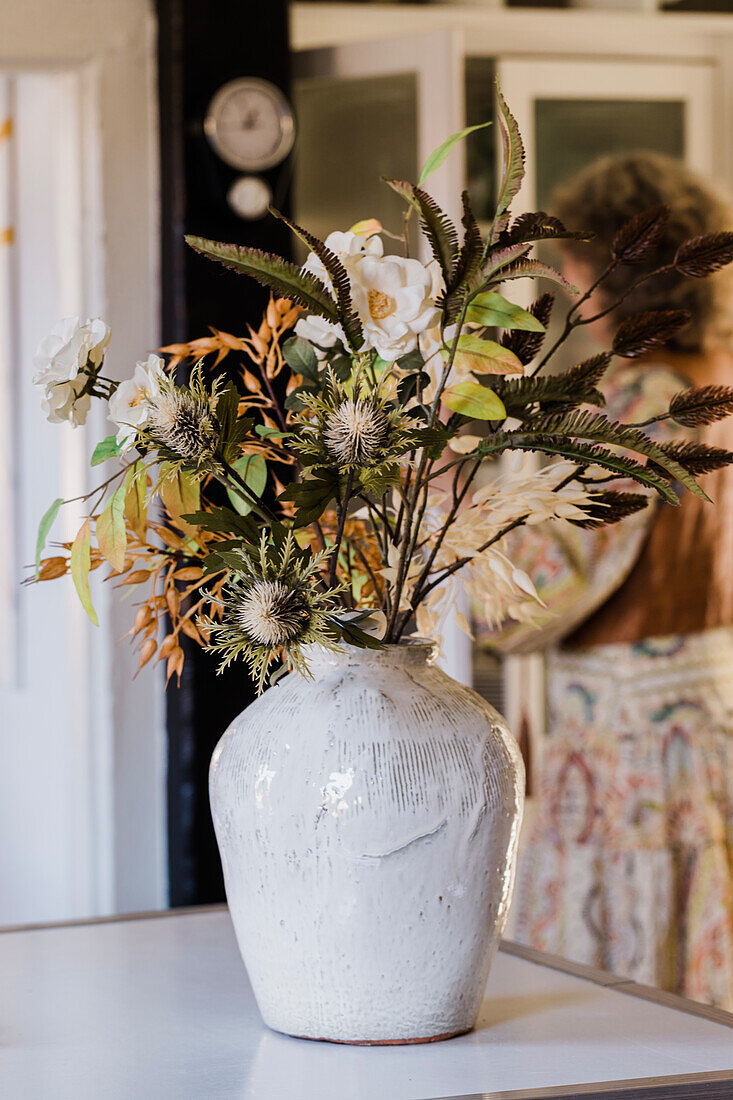 Trockenblumen und Herbstlaub in rustikaler Keramikvase