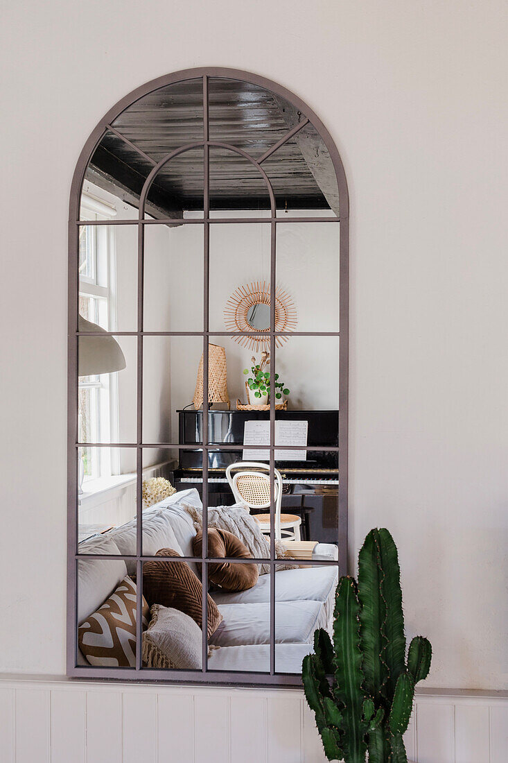 Industrial wall mirror reflects cosy living room with sofa and piano