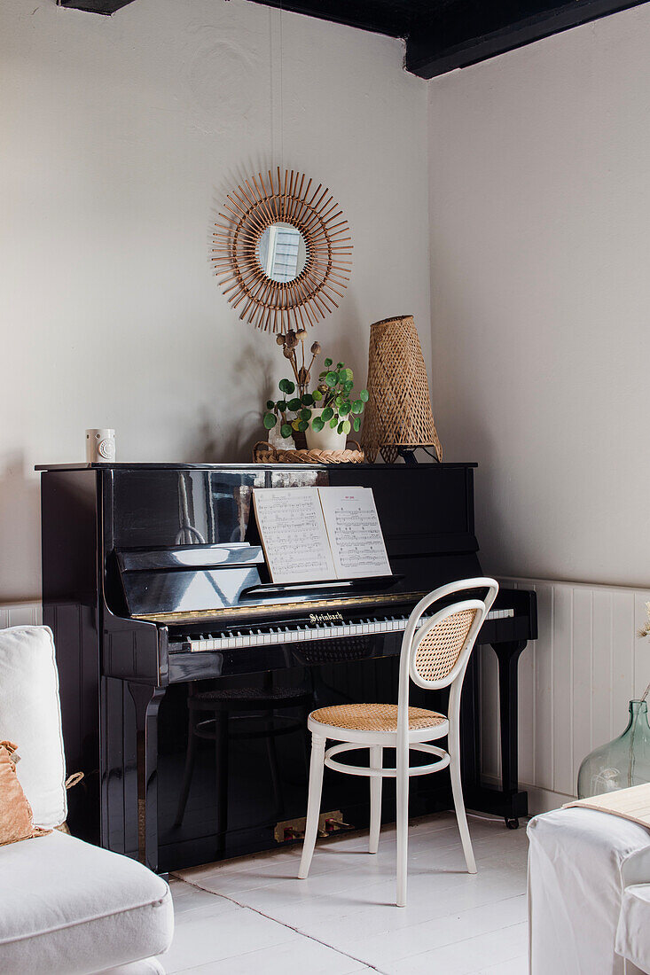 Black piano with sheet music and mirror with rattan frame on white wall