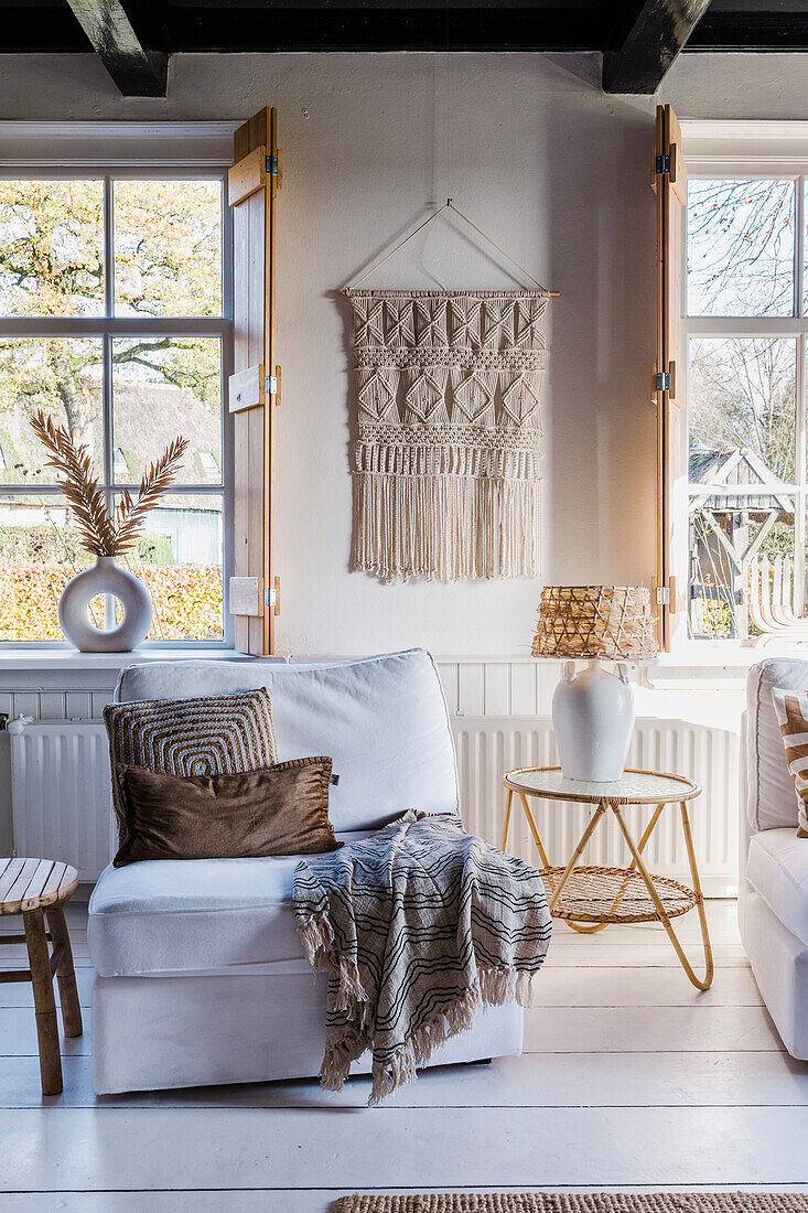 Gemütliche Leseecke mit Wandbehang aus Makramee und dekorativen Kissen im Wohnzimmer