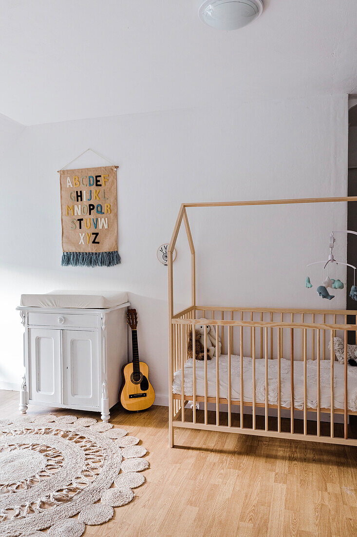 Children's room with wooden cot in the shape of a house, guitar and wall hanging