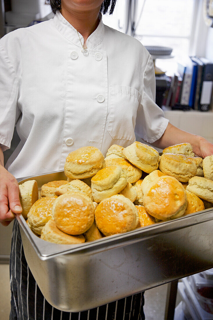 Bäckerin hält ein Blech mit frisch gebackenen Scones