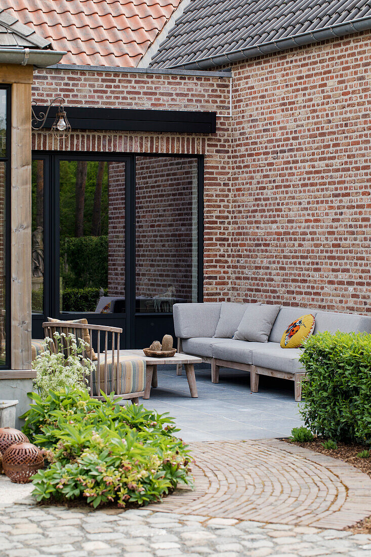 Terrassenbereich mit grauem Sofa und Holztisch vor Backsteinwand