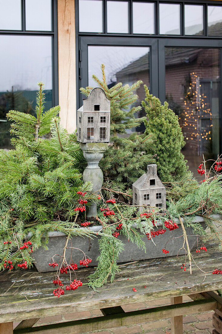 Winterliche Dekoration mit Nadelzweigen, Beeren, und Modellhäusern aus Holz