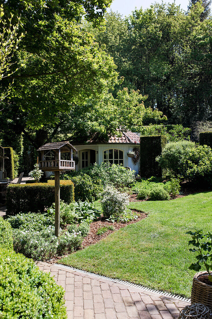 Romantic garden path with bird house and lush vegetation around a garden shed