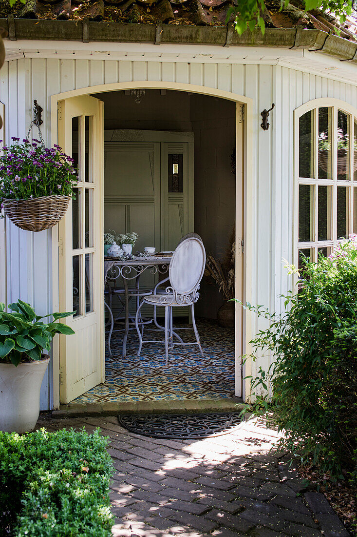 Open arbour with wrought-iron table and chairs, surrounded by green plants