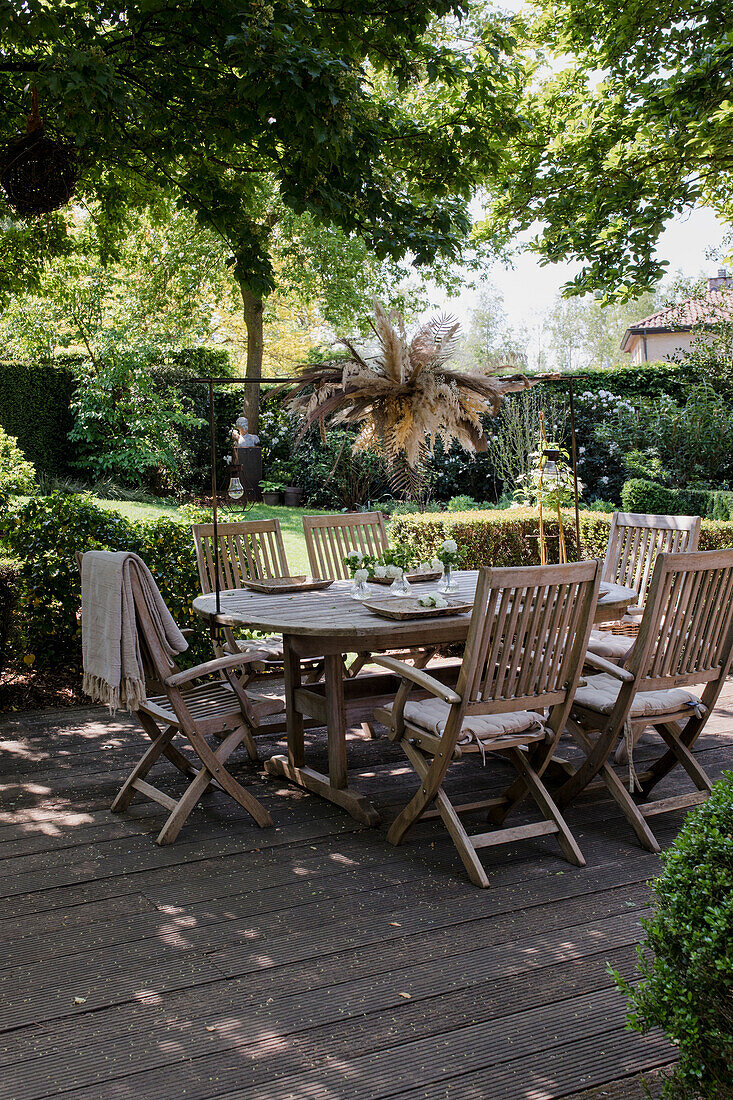 Holztisch mit Stühlen und Trockenblumengesteck auf Terrasse im sommerlichen Garten