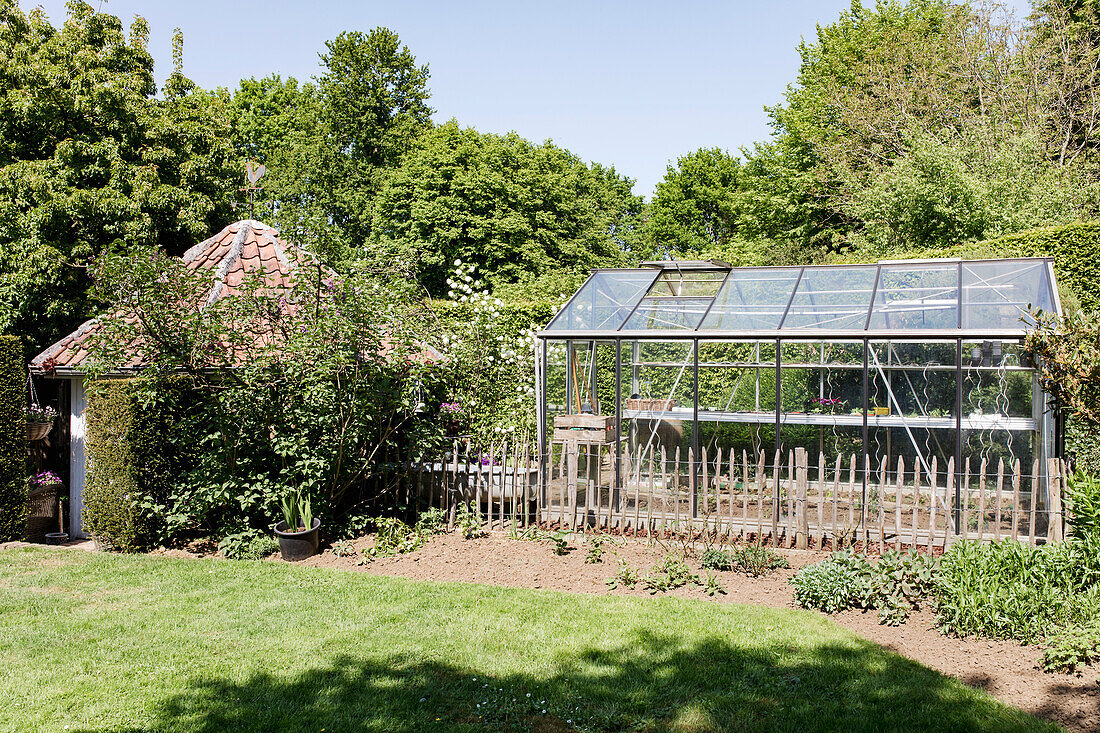 Garten mit Gewächshaus und kleinem Pavillon im Sommer