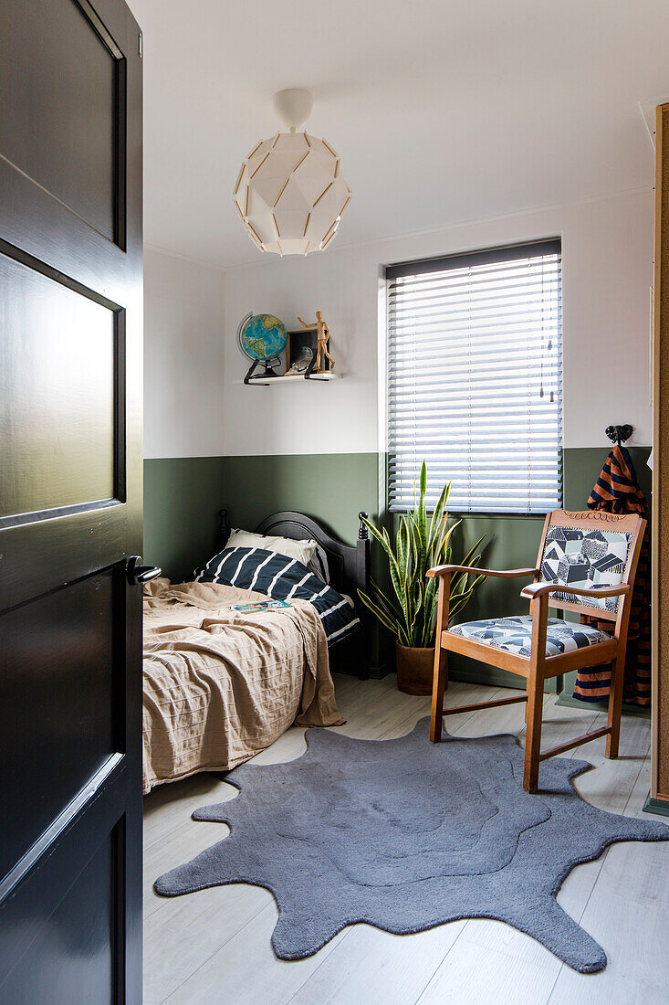 Single bed and reading corner in the bedroom with green wall design and blotchy carpet