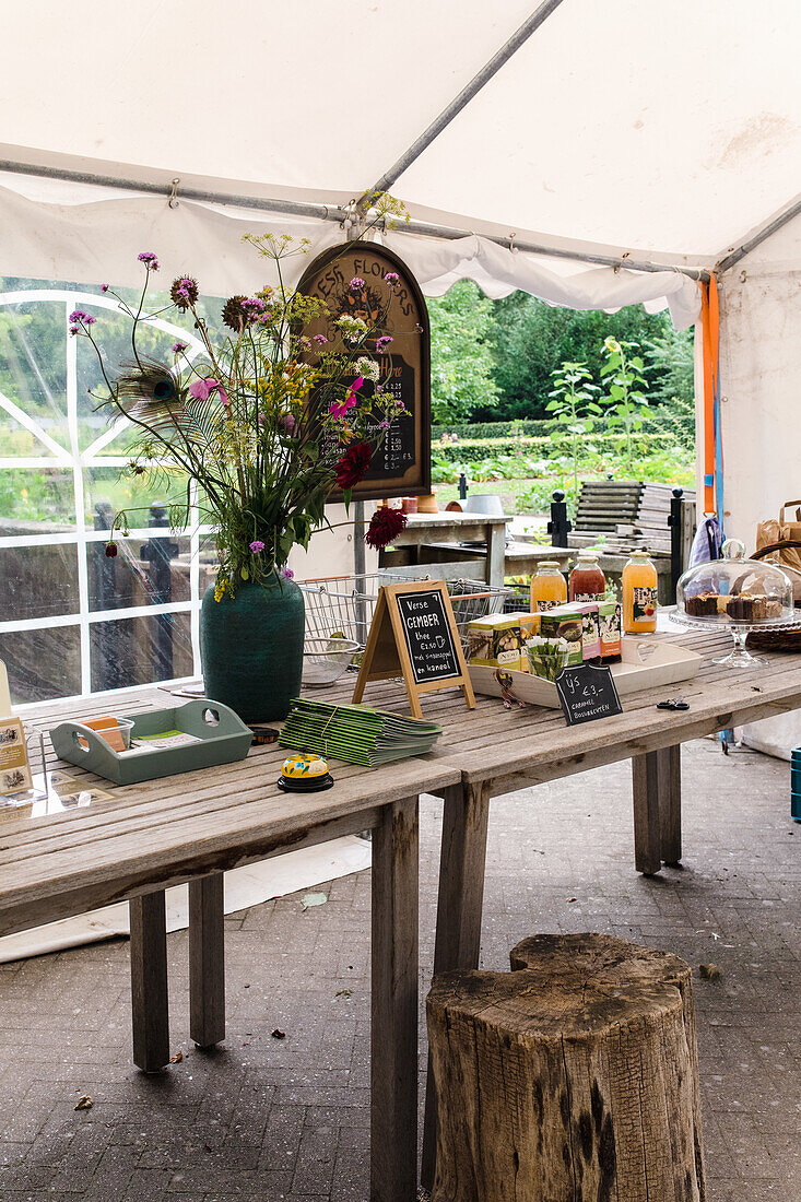 Rustikaler Holztisch mit Blumen, Säften und Gebäck in einem Gartenpavillon