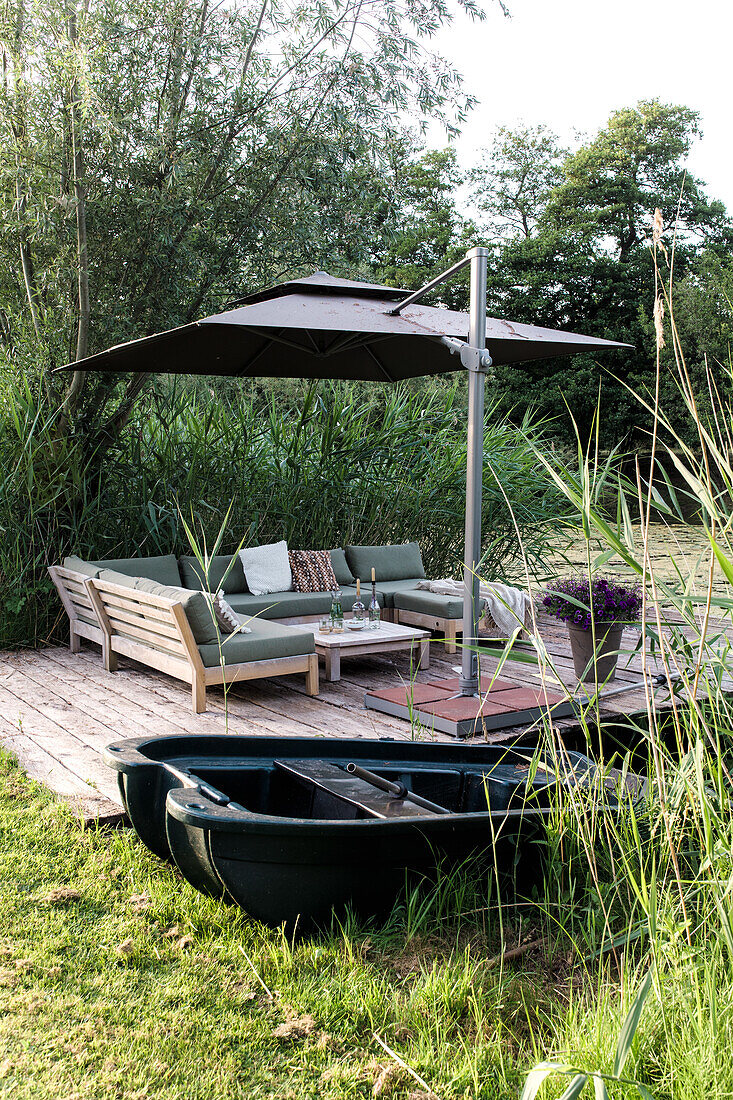 Wooden terrace with seating area and sun umbrella by the water in the garden