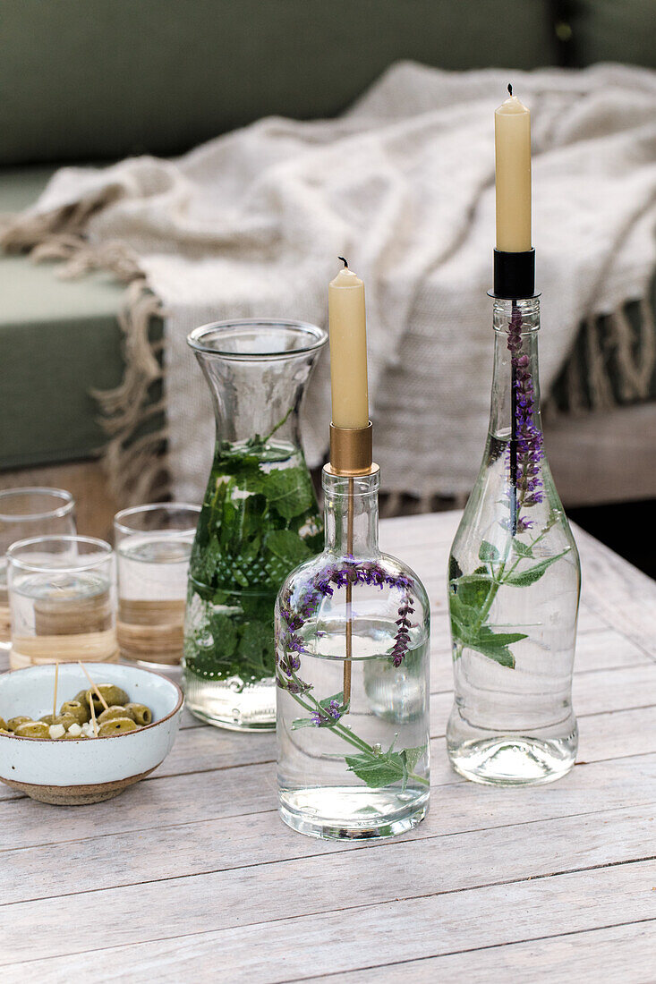 Glass bottles with plants as candle holders on a wooden table in the garden