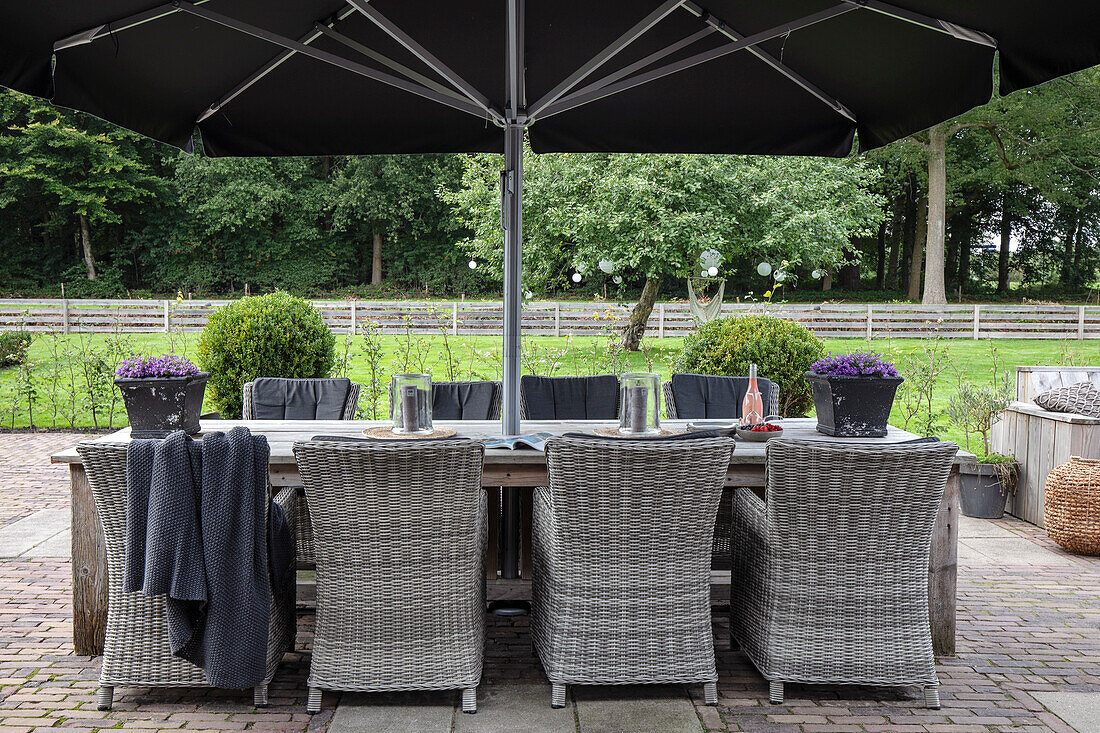 Terrasse mit Rattan-Esstisch, Stühlen und großem Sonnenschirm